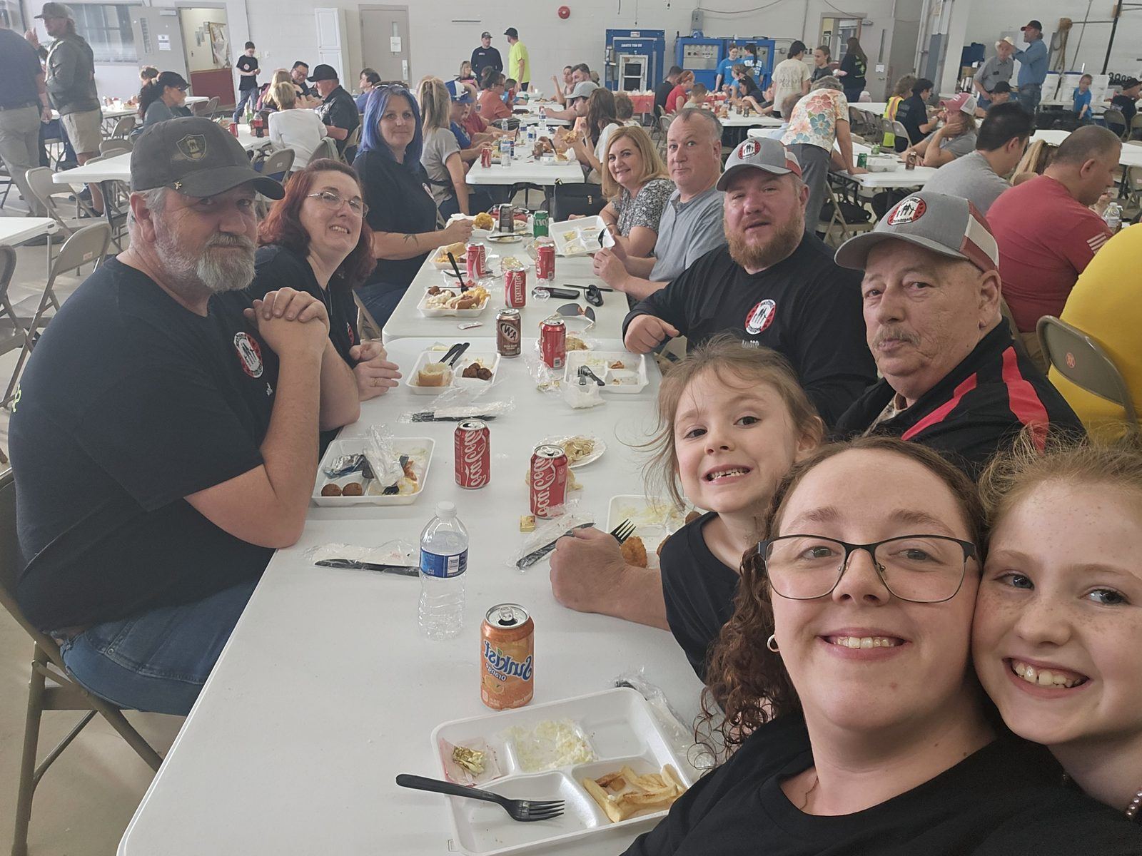 Volunteers and their families share a meal at long tables inside a fire station bay