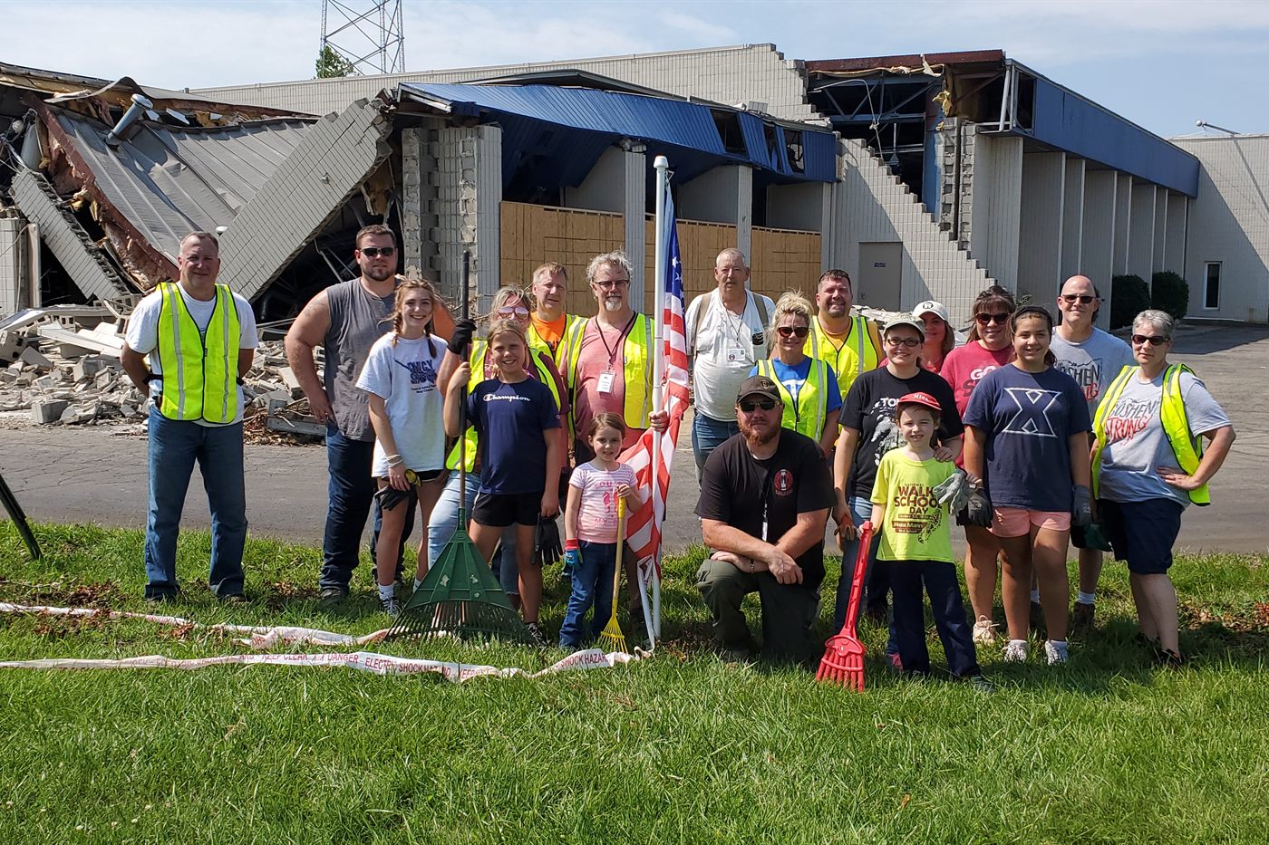 Volunteers and local families gather in front of a storm-damaged building