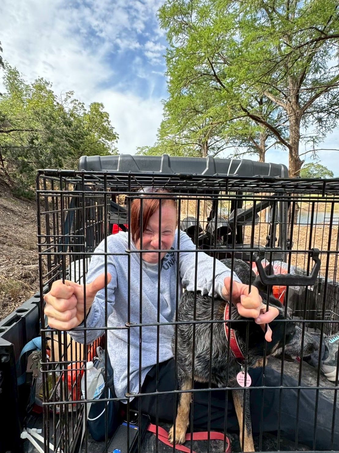 A volunteer gives a thumbs-up from a rescue crate beside a rescued dog during a search and rescue deployment