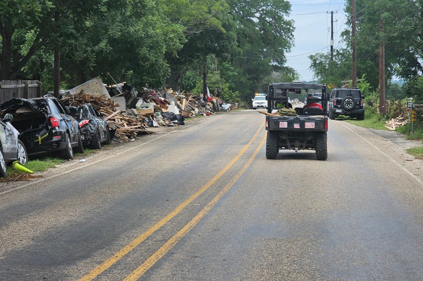 Response vehicles drive down a road lined with storm debris